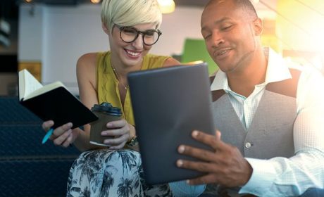 Two people smiling at a tablet while working in the office